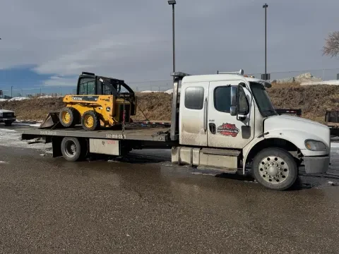 Flatbed tow truck moving small equipment for a hauling job in Langdon